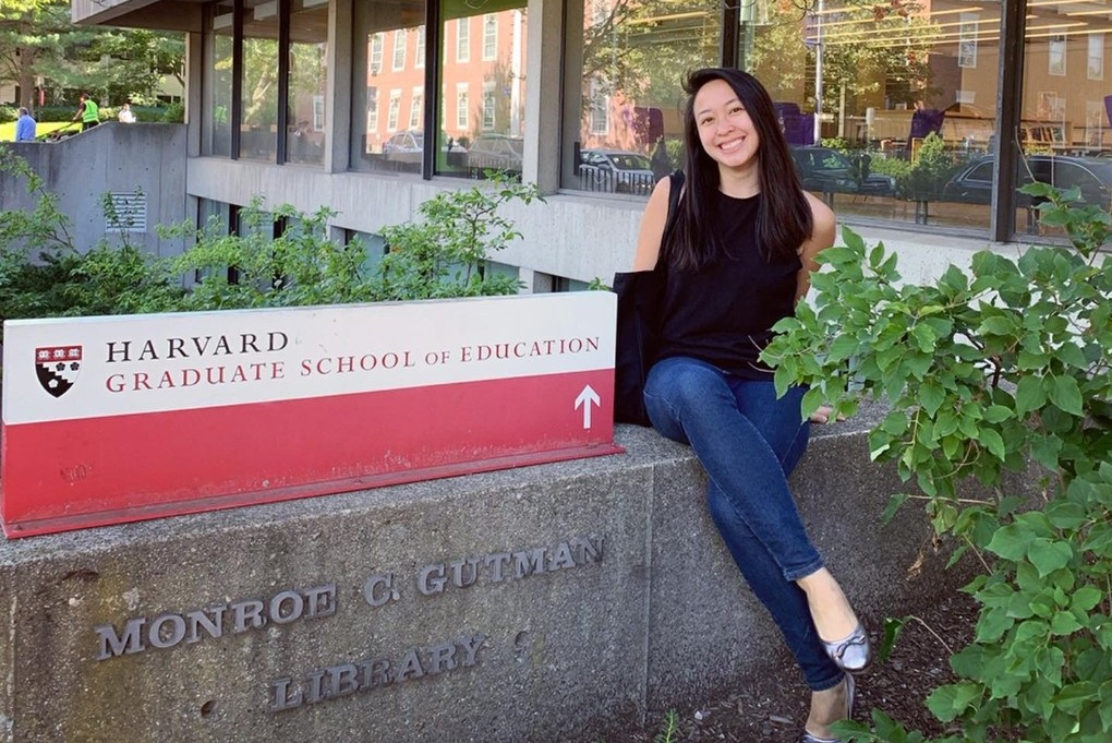 Jiezhen Wu sitting at the HGSE sign in front of the Gutman Library.